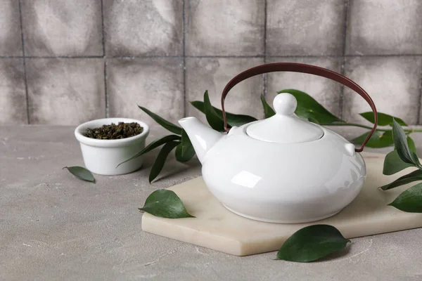 Çaydanlıklı bir pano, bir kase kuru çay ve grunge masasındaki yapraklar gri fayanslara karşı.