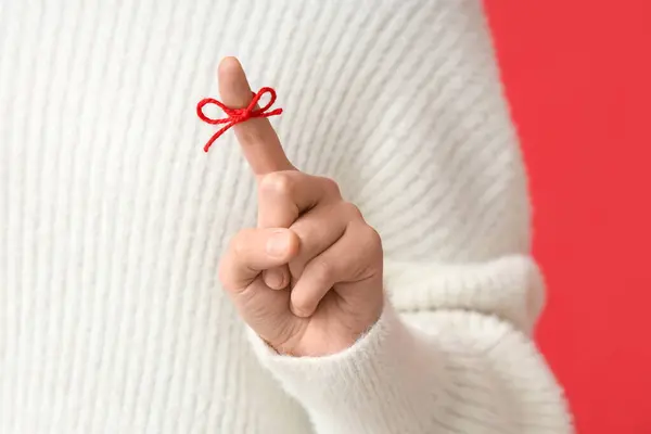 Woman with red bow on index finger against red background. Reminder concept