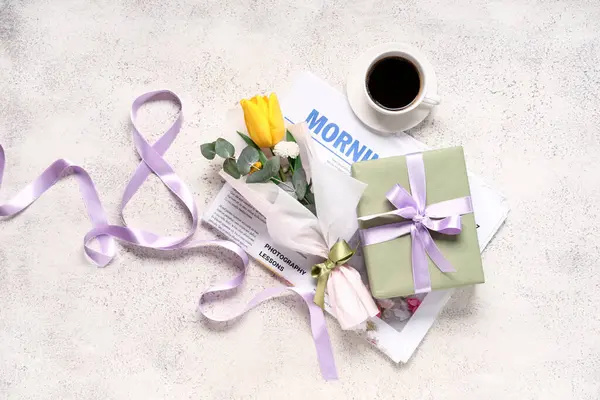 Mini bouquet of beautiful spring flowers in wrapping paper with newspaper, gift box and cup of coffee on white grunge background. International Women\'s Day