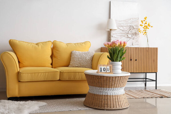 Calendar with date of for International Women's Day and tulips on table in light living room interior