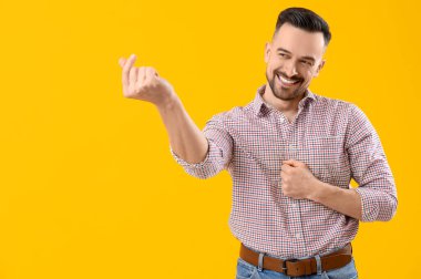 Sarı arka planda parmaklarıyla kalp yapan yakışıklı bir adam.
