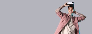 Gri arkaplanda VR gözlük kullanan genç dövmeli bir adam.