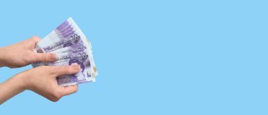 Açık mavi arkaplan üzerinde sterlin banknotlar tutan kadın elleri metin için boşluk ile