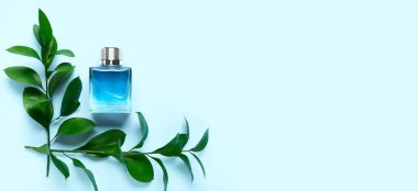 Açık mavi arkaplanda bir şişe parfüm ve dallar.