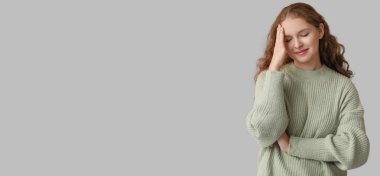 Gri arkaplanda kendini garip hisseden genç bir kadın.