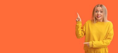 Utanmış genç bir kadın turuncu arka planda mesaj için yeri olan bir şeye işaret ediyor.