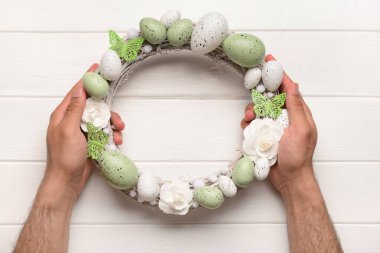 Paskalya çelengini beyaz tahta masada tutan adam.