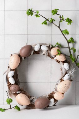 Beyaz duvarın yanında dalları olan yumurta ve tüylerden yapılmış Paskalya çelengi.