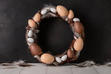 Siyah duvarın yanındaki masada yumurtadan ve tüylerden yapılmış Paskalya çelengi.