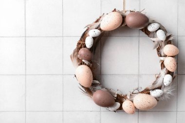 Beyaz duvarda asılı yumurta ve tüylerden yapılmış Paskalya çelengi