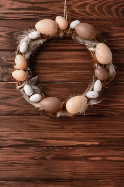 Kahverengi ahşap duvarda asılı yumurta ve tüylerden yapılmış Paskalya çelengi.