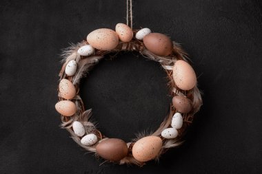 Siyah duvarda asılı yumurta ve tüylerden yapılmış Paskalya çelengi.