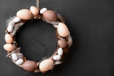 Siyah duvarda asılı yumurta ve tüylerden yapılmış Paskalya çelengi.