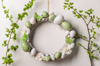 Beyaz duvarda dalları olan çiçeklerden, yumurtalardan ve kelebeklerden oluşan Paskalya çelengi