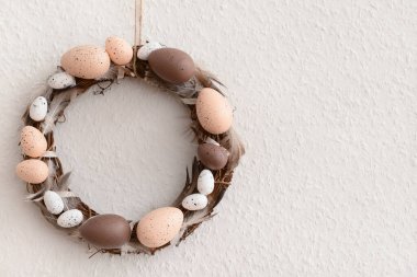 Beyaz duvarda asılı yumurta ve tüylerden yapılmış Paskalya çelengi.