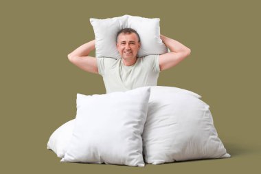 Yumuşak yastıklı olgun bir adam yeşil arka planda oturuyor.