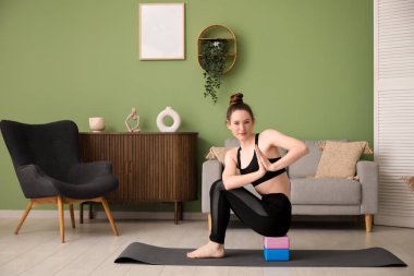 Evde bloklarla yoga yapan genç bir kadın.