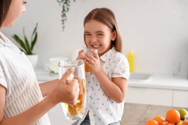 Annesiyle küçük bir kız mutfakta meyve suyu içiyor.