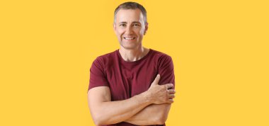 Sarı arka planda katlanmış kolları olan yakışıklı olgun bir adamın portresi.