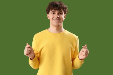 Yakışıklı genç adam yeşil arka planda parmaklarıyla kalp yapıyor.