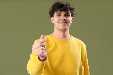 Yakışıklı genç adam yeşil arka planda parmaklarıyla kalp yapıyor.