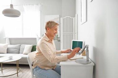 Evde tablet bilgisayarla çalışan olgun bir kadın programcı.