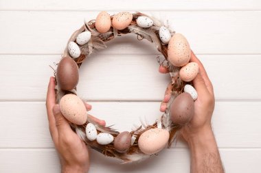 Paskalya çelengini beyaz tahta masada tutan adam.