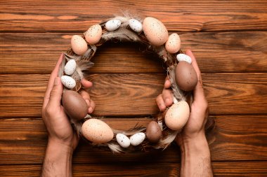 Kahverengi ahşap masada Paskalya çelengi tutan adam.