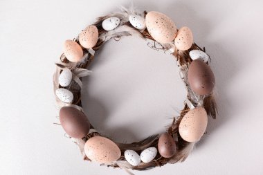 Beyaz arka planda yumurta ve tüylerden yapılmış Paskalya çelengi.