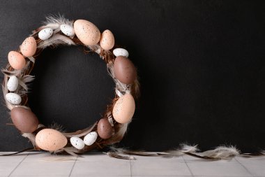 Siyah duvarın yanındaki masada yumurtadan ve tüylerden yapılmış Paskalya çelengi.