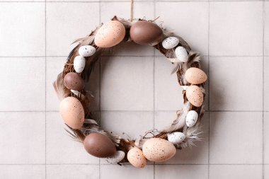 Beyaz duvarda asılı yumurta ve tüylerden yapılmış Paskalya çelengi