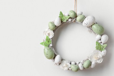 Beyaz duvarda dalları olan çiçeklerden, yumurtalardan ve kelebeklerden oluşan Paskalya çelengi