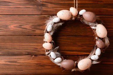 Kahverengi ahşap duvarda asılı yumurta ve tüylerden yapılmış Paskalya çelengi.