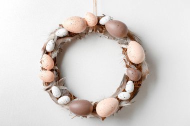 Beyaz duvarda asılı yumurta ve tüylerden yapılmış Paskalya çelengi