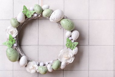 Beyaz duvarda asılı çiçekler, yumurtalar ve kelebeklerden oluşan Paskalya çelengi