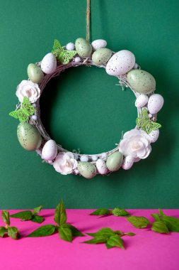 Çiçeklerden, yumurtalardan ve kelebeklerden oluşan Paskalya çelengi koyu yeşil duvarda asılı.