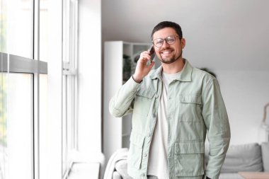 Gözlüklü yakışıklı adam evde cep telefonuyla konuşuyor.