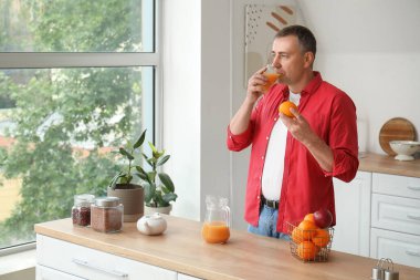 Mutfakta portakal suyu içen olgun bir adam.