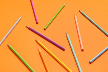 Turuncu arka planda renkli kalemler grubu