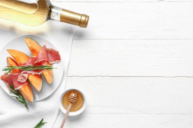 Beyaz ahşap zemin üzerinde jambonlu ve biberiyeli lezzetli kavun tabağı.