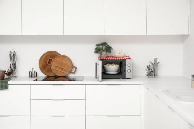 Mikrodalga fırını, elektrikli soba ve beyaz tezgahlı mutfak malzemeleri.