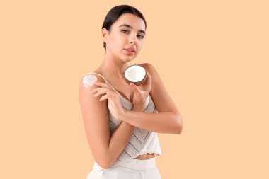 Güzel genç bir kadın bej arka plana hindistan cevizi yağı sürüyor.