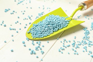 Beyaz ahşap arka planda mavi granüler gübre ile bahçe küreği, yakın plan