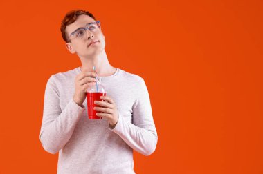 Turuncu arka planda bir bardak gazozu olan düşünceli genç bir kızıl.