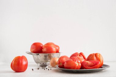 Beyaz arka planda farklı baharatlarla taze olgun domates tabağı ve süzgeci.