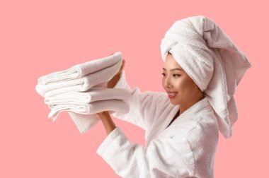 Pembe arka planda bir yığın temiz elbisesi olan bornozlu güzel bir kadın.