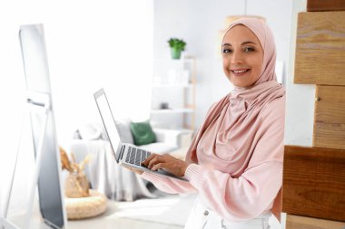 Evde dizüstü bilgisayar kullanan olgun Müslüman kadın.
