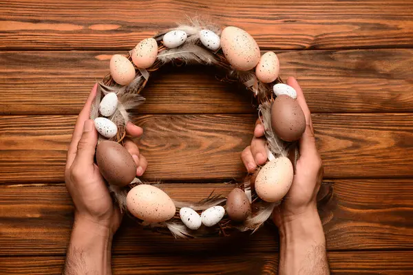 Kahverengi ahşap masada Paskalya çelengi tutan adam.