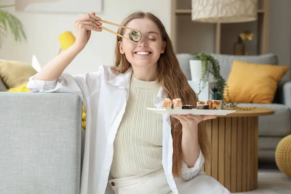 Happy young woman eating sushi in living room