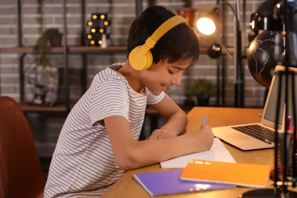 Little boy with headphones studying at home late in evening